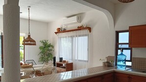 A kitchen with a tiled backsplash, wooden cabinets, a hanging light fixture, and a window with sheer curtains. - Spacious 2 bdrm + A/C, 2 bdrm + A/C in Playacar (Playa del Carmen)
