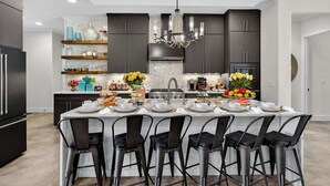 A modern kitchen with dark cabinets, a central island with bar stools, and a chandelier. - Lakeshore Landing | Concierge Services (Kingsland)