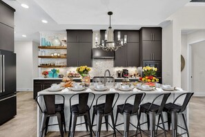 Une cuisine moderne avec des meubles de couleur sombre, un îlot central doté de tabourets de bar et un lustre.