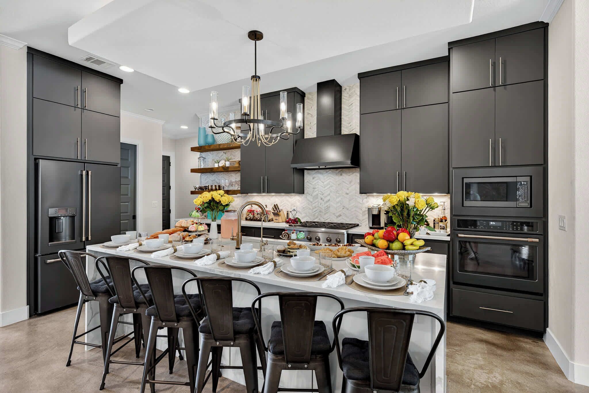 A modern kitchen with dark cabinetry, a central island with seating, a built-in oven, and a microwave.