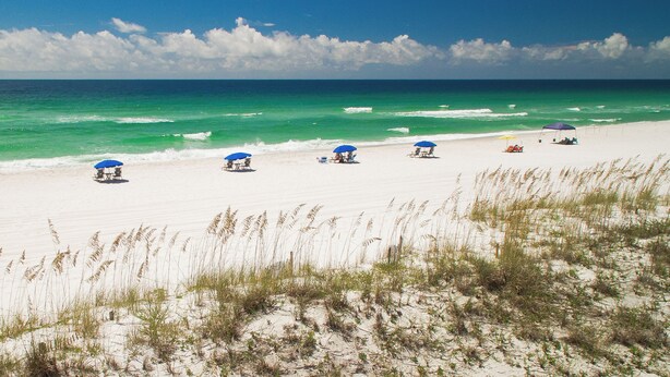 A beach with white sand, clear turquoise water, and a few umbrellas providing shade.