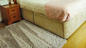 Una cama bien hecha con cabecera de madera, una mesita de noche con lámpara y una alfombra estampada sobre piso de madera.