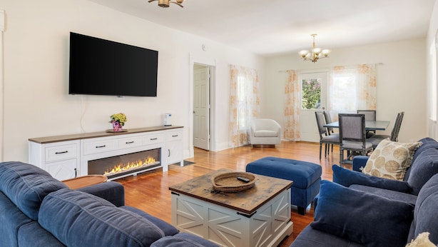 A living room with a fireplace, a TV mounted on the wall, a dining area with a table and chairs, and a sofa set.