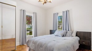 A bedroom with a bed, a nightstand, a wardrobe, and a window with curtains.