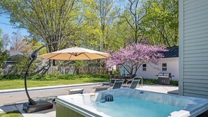 A backyard with a hot tub, a patio table, and an umbrella.