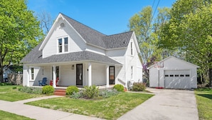 A two-story white house with a front porch, a garage, and a well-maintained lawn.