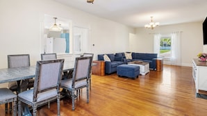 A spacious living area with a dining table and chairs, a blue sofa, and a kitchen area.