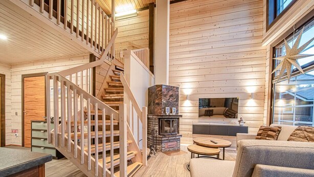 A wooden interior with a staircase, a fireplace, a sofa, and a dining area.