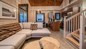 A modern log cabin interior with a living area featuring a sofa, a round wooden coffee table, and a remote control on it.
