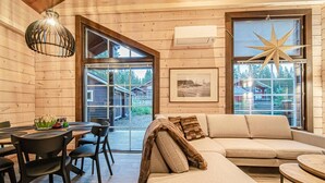 A cozy cabin interior with a wooden interior, a dining area, a sofa, and large windows offering a view of the outdoors.