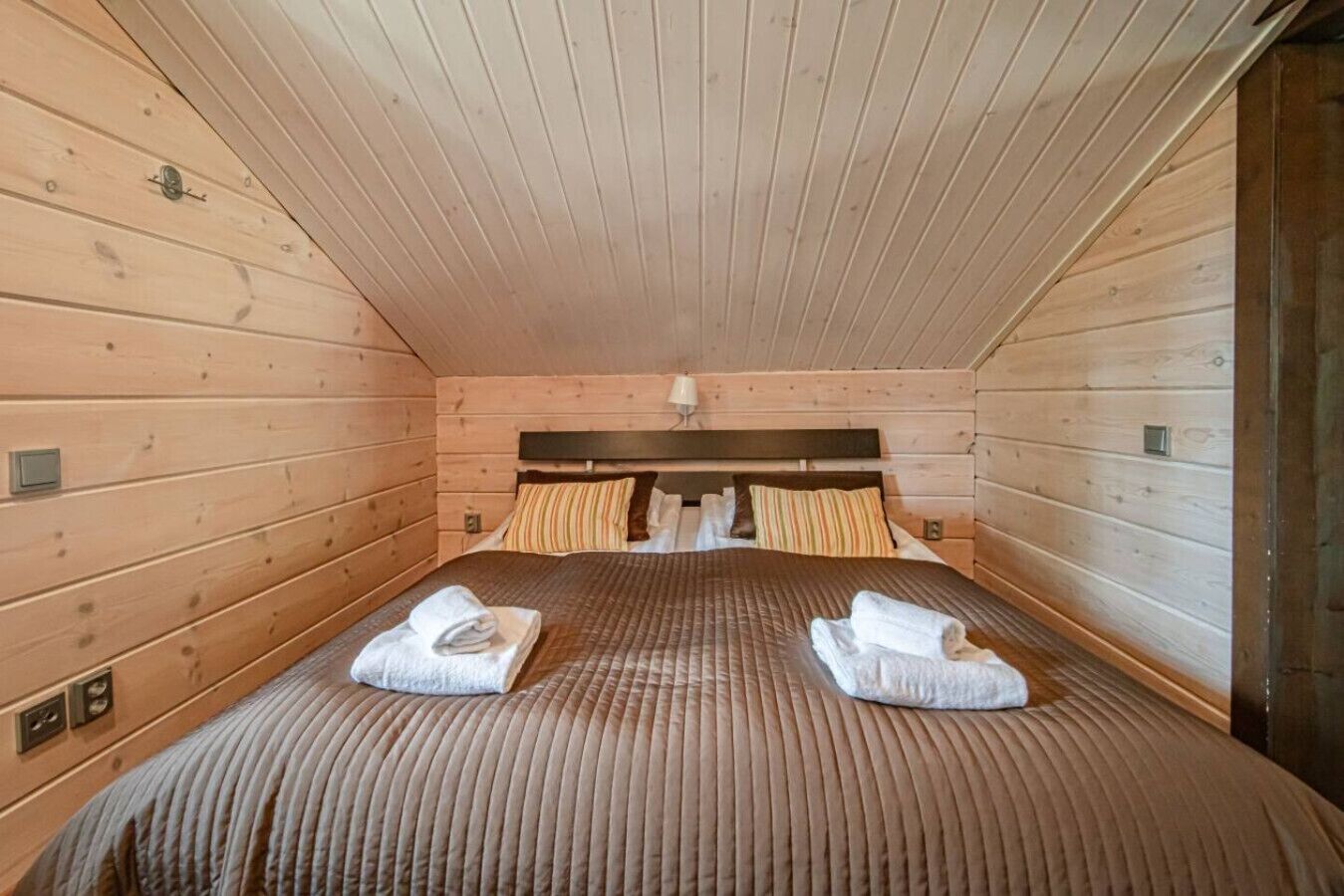 Une chambre dans un chalet en bois, avec un lit, des oreillers et une tête de lit.