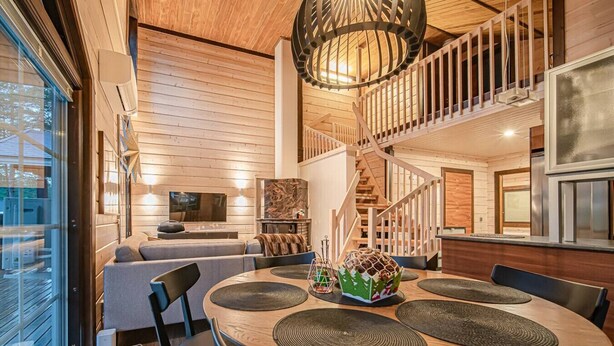 A modern interior with a wooden floor, a round dining table with chairs, a sofa, a TV, and a staircase.