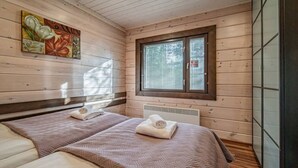 A wooden cabin room with two beds, a window, and a painting on the wall.
