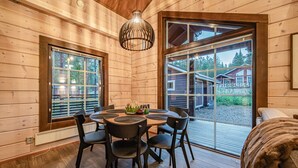 A wooden cabin interior with a dining table and chairs, large windows, and a view of the outside.
