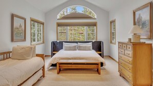 A bedroom with a large bed, a smaller bed, a dresser, and a window with a view of trees.