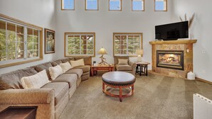 A living room with a sectional sofa, a round coffee table, a fireplace, and a flat-screen TV mounted above it.