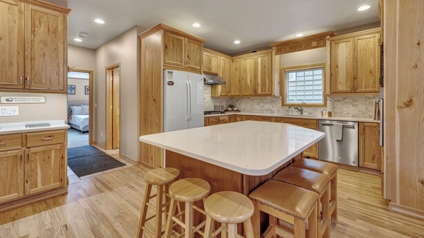 A kitchen with wooden cabinets, a large island with stools, stainless steel appliances, and a window with blinds.