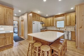 Une cuisine avec des meubles en bois, un grand îlot central doté de tabourets, des appareils électroménagers en acier inoxydable et une fenêtre avec des stores.