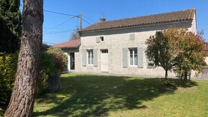 A stone building with a tiled roof, a grassy yard, and a tree. - GITE DES VIGNES (Archiac)