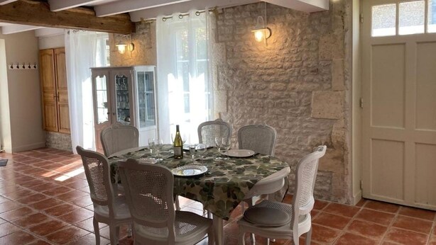 A dining area with a round table, six chairs, and a stone wall. - GITE DES VIGNES (Archiac)