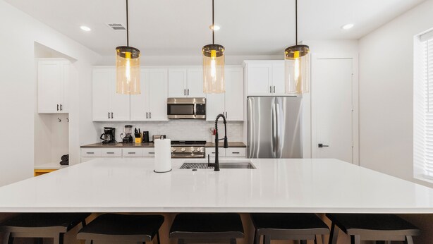 A modern kitchen with white cabinetry, stainless steel appliances, and a central island with bar stools.