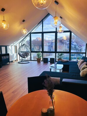 A modern loft bedroom with a large skylight, a hanging chair, and a cozy seating area.