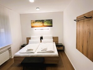 A neatly made bed with white linens, a bedside table with a lamp, and a wall-mounted picture of a tree.