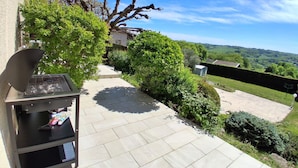 Une terrasse avec un barbecue, un chemin et une vue sur la campagne.