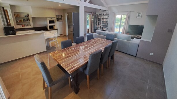 Une cuisine moderne dotée d’un îlot central, un coin repas avec une table en bois et un salon avec un canapé et un téléviseur.
