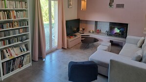 Un salon avec un canapé blanc, un téléviseur, une cheminée et une bibliothèque remplie de livres.