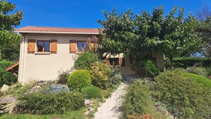 Une maison à deux étages, avec un toit recouvert de tuiles, des volets en bois et un escalier en pierre menant à l’entrée.
