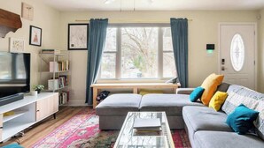 A living room with a sofa, a coffee table, a TV, and a bookshelf. - Porch & Yard, Spacious & Cozy, Close to Downtown! (Raleigh)