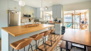 A modern kitchen with a wooden island, bar stools, stainless steel appliances, and a view to the outdoors. - Porch & Yard, Spacious & Cozy, Close to Downtown! (Raleigh)
