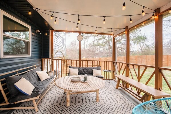 A covered outdoor seating area with a round wooden table, benches, and string lights.
