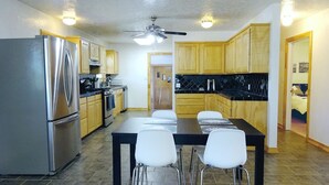A modern kitchen with stainless steel appliances, wooden cabinets, and a dining area with four white chairs. - Clean, fully stocked home in Mitchell. (Mitchell)
