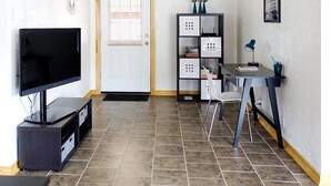 A modern living room with a flat-screen TV, a small table with a lamp, a chair, and a decorative shelf. - Clean, fully stocked home in Mitchell. (Mitchell)