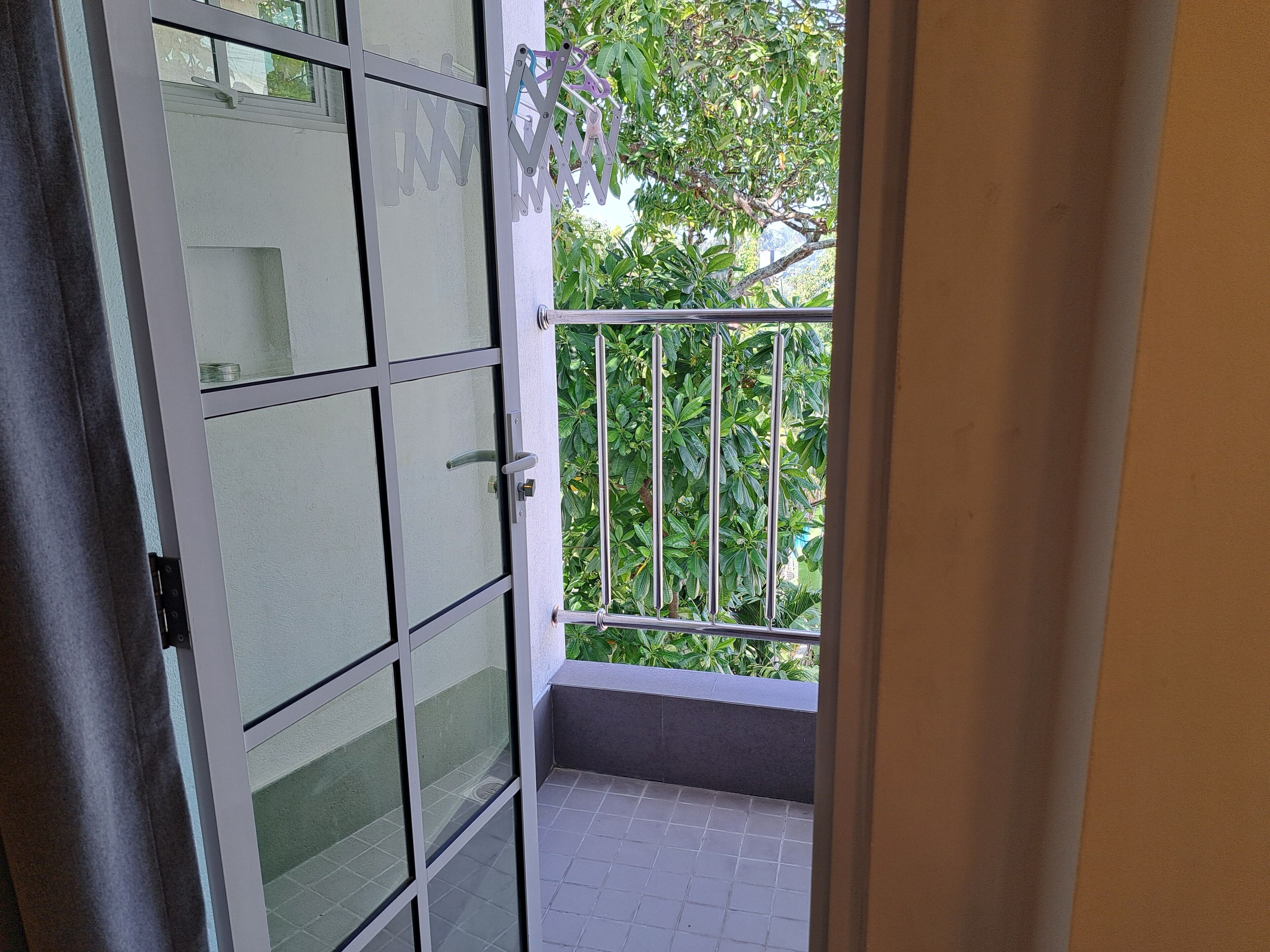 A view of a balcony with a metal railing, a glass door with frosted panels, and a tiled floor.