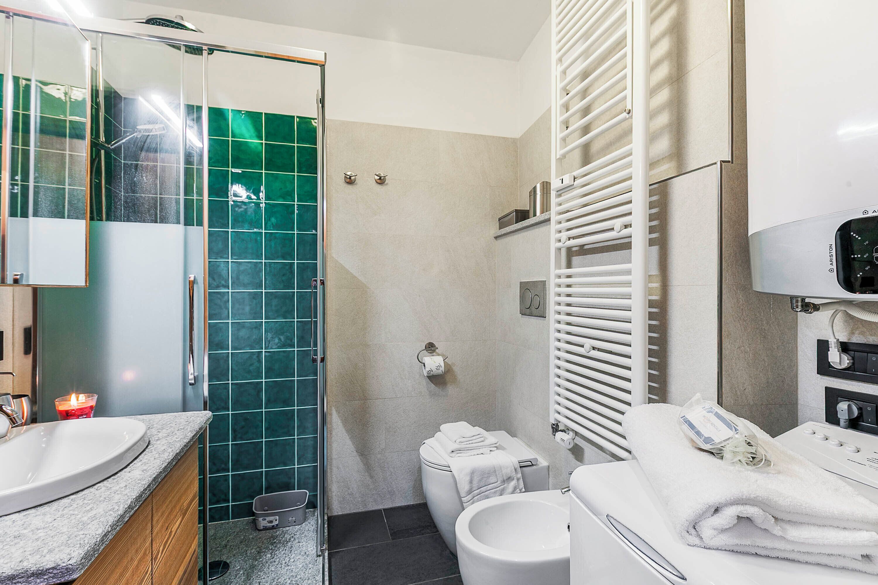 A bathroom with a glass shower enclosure, a white toilet, a sink with a mirror, and a towel rack.