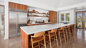 Una cocina moderna con un refrigerador de acero inoxidable, armarios de madera, una isla central con taburetes de bar y un ventanal que proporciona luz natural.