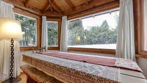 A cozy room with a wooden ceiling, a large bed with patterned bedding, a bedside table, and a lamp. - Mountain cabin with large garden and lots of sun. (San Carlos de Bariloche)
