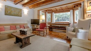 A cozy living room with a wooden ceiling, a sofa with striped cushions, a red armchair, a wooden coffee table, a television, and a piano. - Mountain cabin with large garden and lots of sun. (San Carlos de Bariloche)