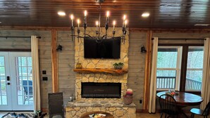 A cozy living room with a stone fireplace, a television mounted above it, and a dining area with a round table and chairs.