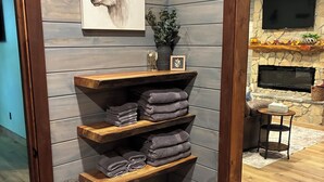 A corner of a room with wooden walls, a fireplace, a mounted TV, and a shelf with folded towels.