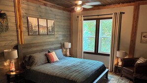 A bedroom with a large bed, two bedside lamps, a window with curtains, and a ceiling fan.