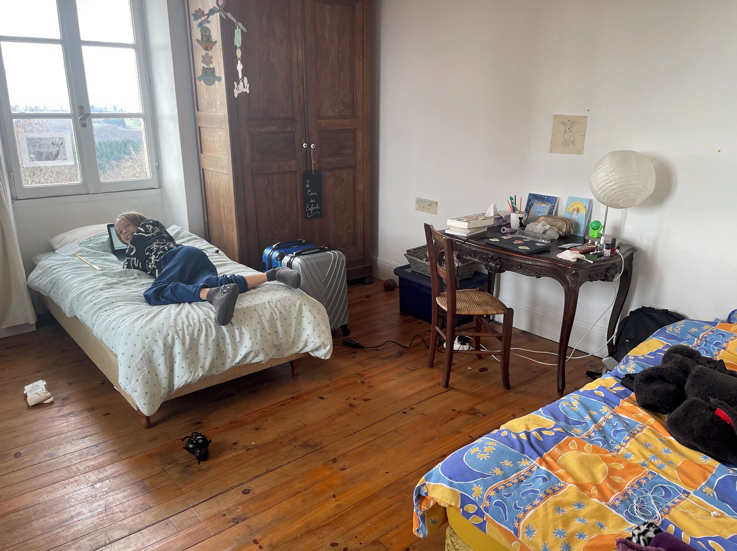 Un dormitorio con cama, escritorio con lámpara, maleta y silla.