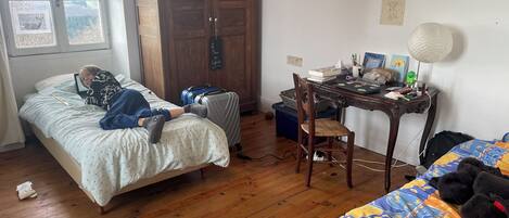 Un dormitorio con cama, escritorio con lámpara, maleta y silla.