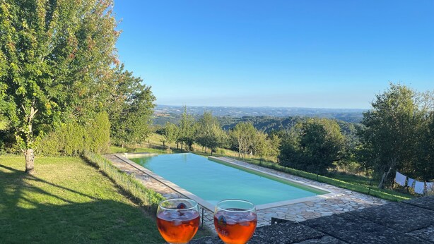 Eine Steinsitzbank mit Blick auf einen Swimmingpool und eine malerische Aussicht auf Bäume und Hügel.