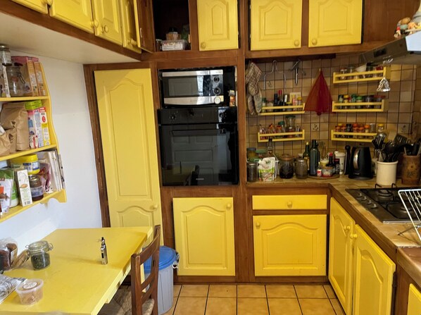 A kitchen with yellow cabinets, a built-in oven, and various kitchen items on shelves. - To be awakened by the sound of birdsong (Sabadel-Latronquière)