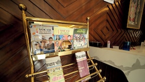 A magazine rack with various publications, a counter with a white surface, and a wooden wall with a geometric pattern. - Staykart Z (Bhilwara)