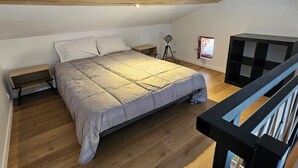 A bedroom with a bed, wooden flooring, a small bedside table, a lamp, and a black TV stand. - Winegrower's house, private courtyard, 4 people/2 beds (Prompsat)